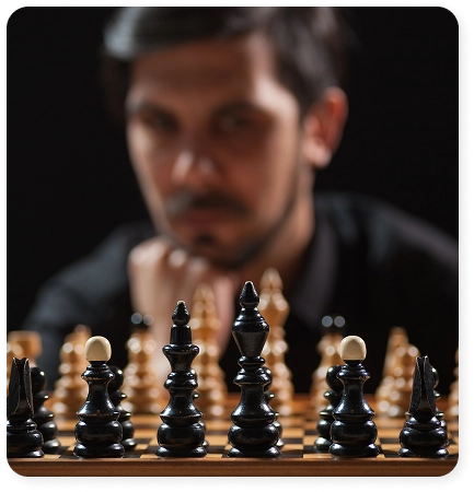 Een man zit geconcentreerd achter het schaakbord te spelen, met de zwarte stukken op de voorgrond