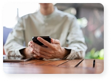 Een man houdt een smartphone vast aan tafel; close-up van zijn handen met het mobiele apparaat